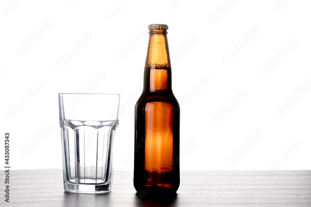 A brown beer bottle with no label with an empty glass on a table A brown beer bottle with no label with an empty glass on a table