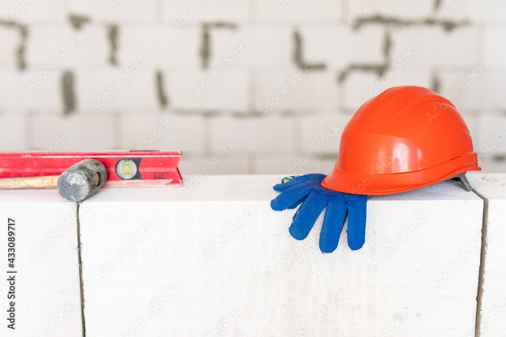 Fototapeta premium Builder tools lays aerated concrete block at a construction site. Objects. Hemlet, gloves, water lavel, hammer on brick wall
