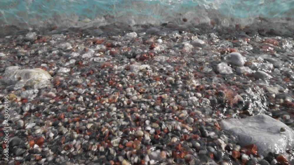 Slow motion shot of waves crushing on pebble beach. Sea beach with clear turquoise water, surf. Low angle shooting Slow motion shot of waves crushing on pebble beach. Sea beach with clear turquoise water, surf. Low angle shooting