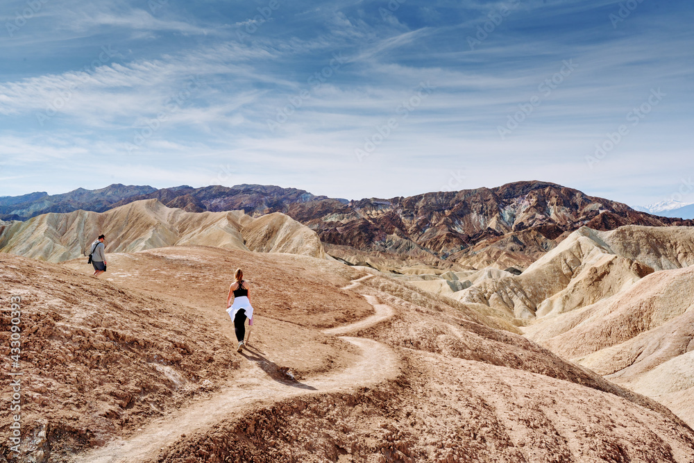 A family hike from Zabriskie Point in Death Valley national park in california. Huge sand dunes, terracotta mountains and hazy horizons are shining against clear blue sky in the midday sun.