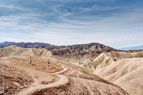 A family hike from Zabriskie Point in Death Valley national park in california. Huge sand dunes  terracotta mountains and hazy horizons are shining against clear blue sky in the midday sun.