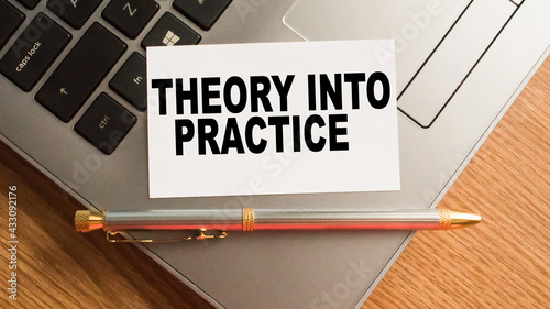 A notebook with text THEORY INTO PRACTICE on the office desk, a laptop with stationery. A blank notepad for entering a copy or text. business