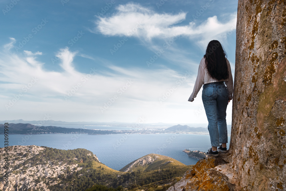 Naklejka premium young woman standing on a cliff in front of a bay