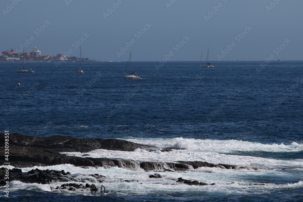 Waves crashing on rock with boats in the background

