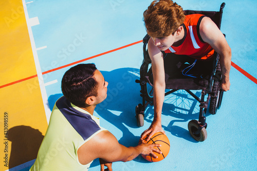 Fototapeta latin young man using wheelchair and playing basketball with a friend in Mexico,
