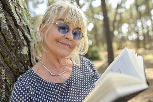 Mature woman doing a break outdoors in a park, setting on the floor and reading a book