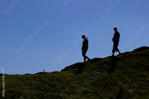 Silhouettes of two people going down the hillside. Dark landscape