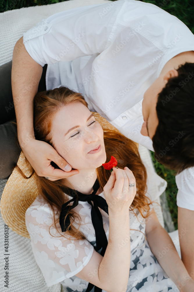 Young girl eating fresh sweet strawberry on a picnic is resting lying on her partner. Close-up of a happy woman having breakfast in nature. Young girl eating fresh sweet strawberry on a picnic is resting lying on her partner. Close-up of a happy woman having breakfast in nature.