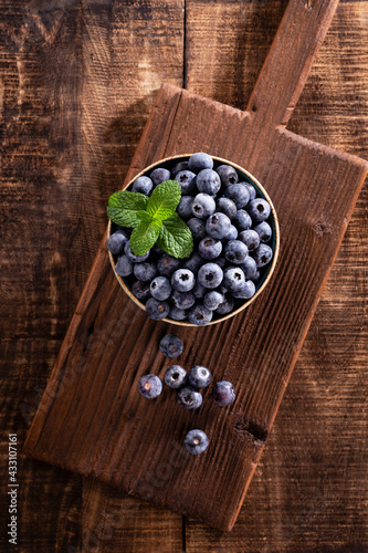 Bowl of fresh blueberries on rustic wooden board. Organic food blueberries and mint leaf for healthy lifestyle.