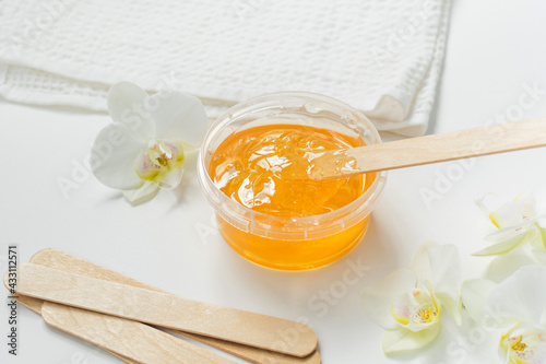 Sugar paste or wax honey in a transparent jar and white orchid on a white background. Sugaring. Depilation and beauty concept. Waxing.