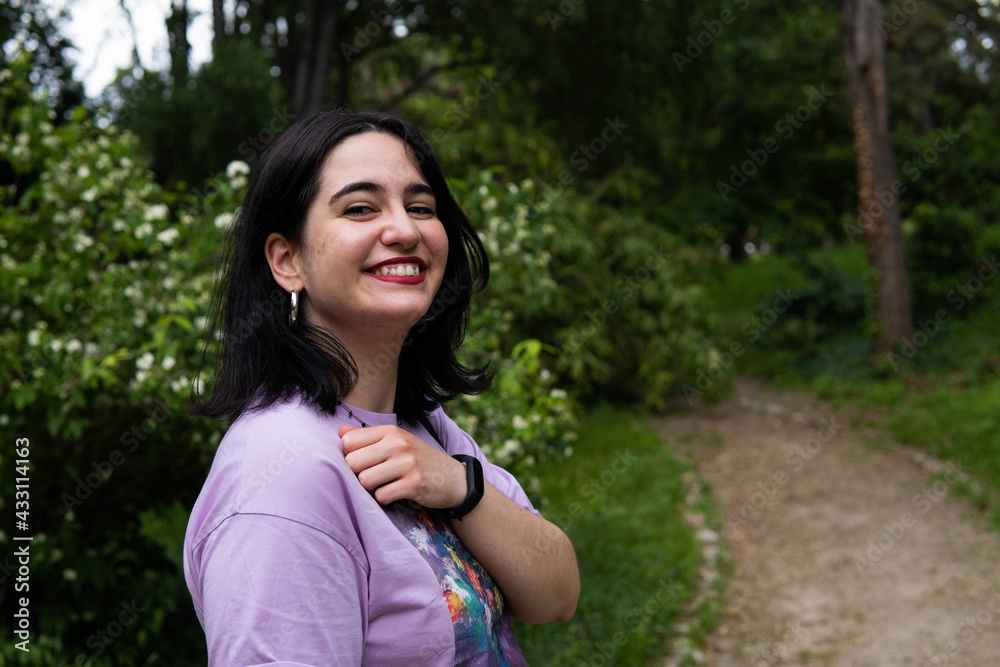 Photo of an attractive woman with black hair in the middle of nature during spring time, walking around and smiling during a sunny day Photo of an attractive woman with black hair in the middle of nature during spring time, walking around and smiling during a sunny day