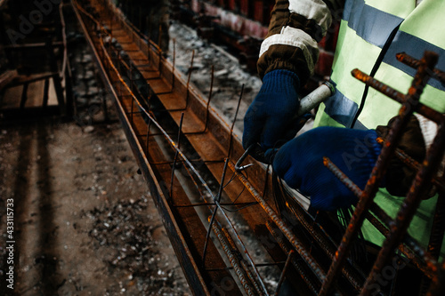 a worker at a reinforced concrete plant in gloves makes rebar