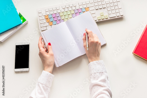 Desk in the office, a woman writes something in a notebook, female hands, office desk on a white background, top view, flat lay
