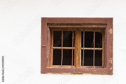 Window with a wooden frame on a white wall of the house. There is a grille in the windows. There are cobwebs around the window.