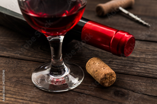 Bottle of red wine with a glass of red wine and cork on an old wooden table. Close up view, focus on the glass of red wine