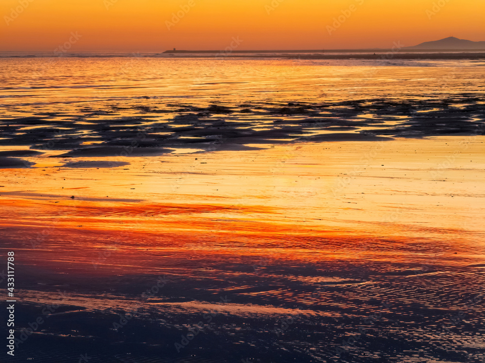 

Sunset on beach at low tide with reflections of the orange sky in the water