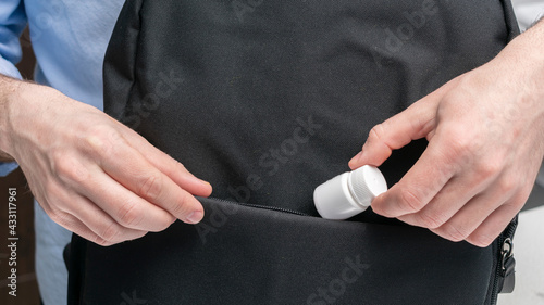 Man puts container of pill in a backpack, male hands, cropped image, close-up