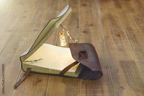 Open book with a miniature flashlight lies on a wooden table. Close-up.