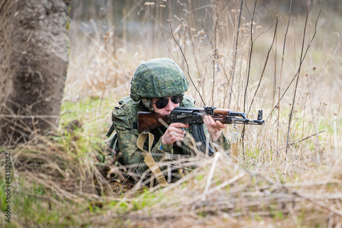 portrait of a fully equipped soldier taking aim with a rifle on battlefield in the midst of dry grass.