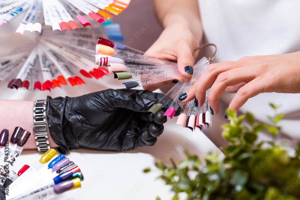 Fototapeta premium Master with a customer in beauty salon choose the color of gel in manicure and pedicure cabinet. Set of different nail polish colours on multicolor nail polish palette for client choice. Nail art