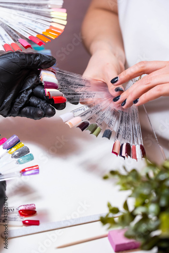 Master with a customer in beauty salon choose the color of gel in manicure and pedicure cabinet. Set of different nail polish colours on multicolor nail polish palette for client choice. Nail art 