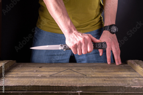 The man is holding a large folding knife. A man in jeans and a T-shirt.