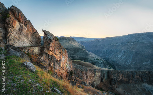 Colorful morning landscape with silhouettes of big rocky mountains and epic deep gorge. Dirt mountain road, serpentine with a cliff and a beautiful panoramic view of the gorge