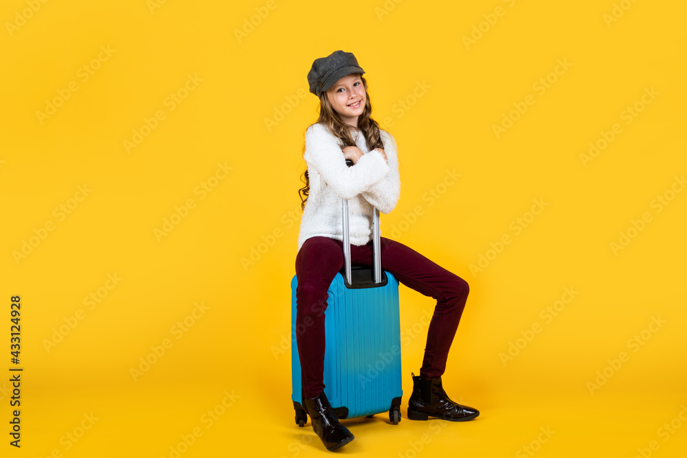 cheerful child in headwear with valise for travelling on yellow background, vacation cheerful child in headwear with valise for travelling on yellow background, vacation