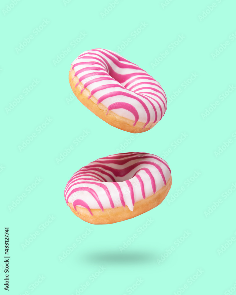 Two pink glazed  donut flying on neo mint background. Levitation concept food.