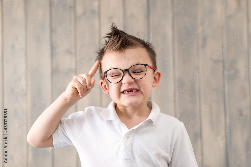 Portrait of little boy laughing in glasses and white T-shirt at wooden background. Preparation for school. having an idea. No milk teeth. Low vision, eyesight measurement. Back to school. Portrait of little boy laughing in glasses and white T-shirt at wooden background. Preparation for school. having an idea. No milk teeth. Low vision, eyesight measurement. Back to school.