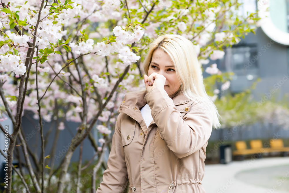 Young pretty woman sneezing in front of blooming tree. Spring allergy concept Young pretty woman sneezing in front of blooming tree. Spring allergy concept