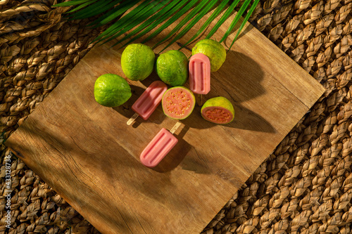 Guava Popsicle with grava fruits on a wood base, sunlight, palm leaf, top view