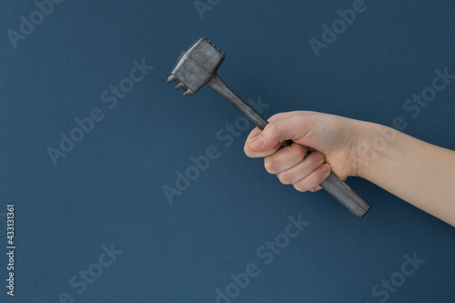Close up image of female hand holds kitchen iron hammer for food preparation on dark green background, copy space. Creative food concept