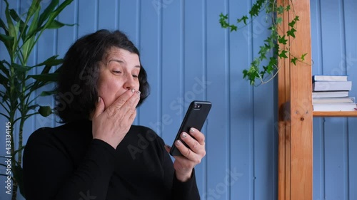 Woman looks at the smartphone screen and feels overjoyed, win in lottery, receive a good news. A mature lady in triumph at home
