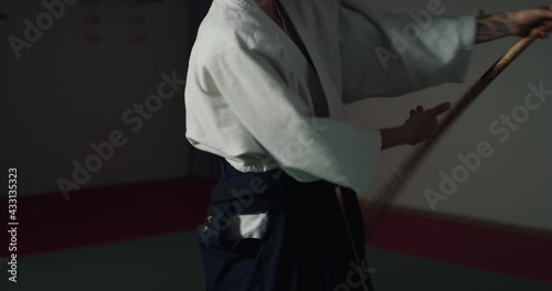 Cinematic shot of budokai fighter master practicing with wooden sword Aikido training in modern Japanese martial arts school. Concept of sports and recreation, philosophy, defense, religious beliefs.