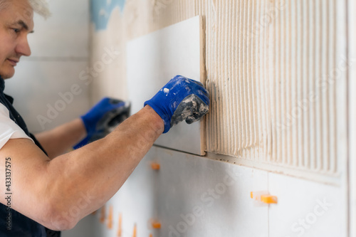 Proffesional tiler installing wall tile at home. Workers laying tiles on a bathroom wall. DIY, Do it yourself concept. House improvement. Repair renovation work. Selective focus, copy space