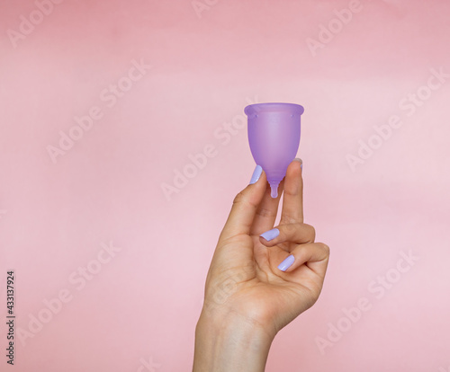 woman's hand holding a purple menstrual cup, on a plain pink background photo