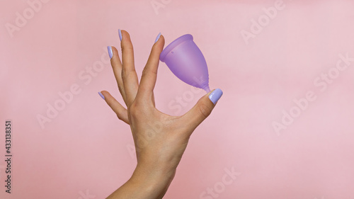woman's hand holding a purple menstrual cup, on a plain pink background