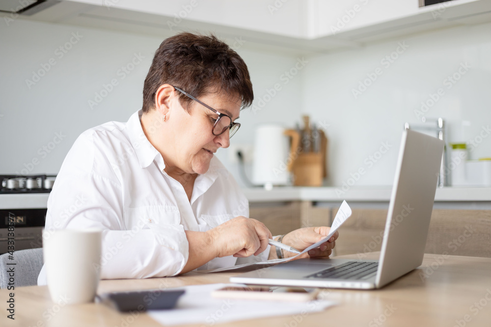 mature middle aged business woman using laptop working on computer with documents, sitting at desk. mature middle aged business woman using laptop working on computer with documents, sitting at desk.