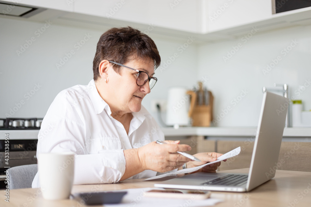 mature middle aged business woman using laptop working on computer with documents, sitting at desk. mature middle aged business woman using laptop working on computer with documents, sitting at desk.