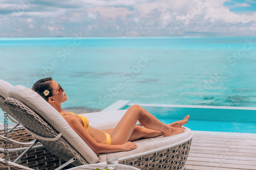 Fotografie, Obraz Luxury vacation in paradise Bora Bora high end resort hotel bikini woman relaxing lying on lounger sunbathing by the swimming pool at overwater villa suite