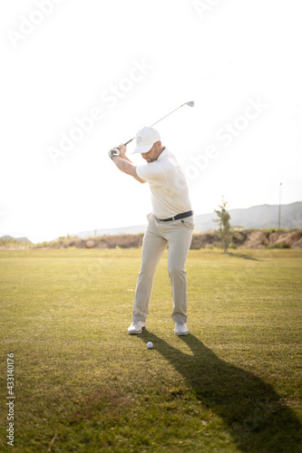 Golf player making a perfect swing on the golf course in the sunset.