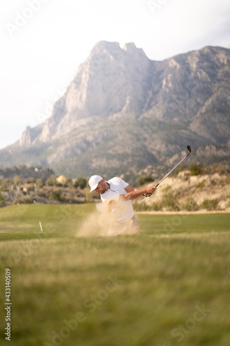 Golfer kicking the ball out of the bunker on the golf course at sunset