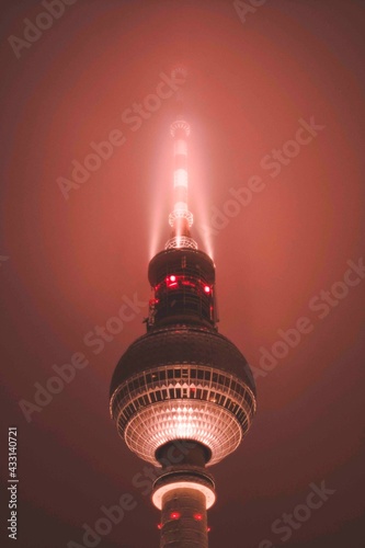 Famous Alexanderplatz TV Tower of Berlin, Germany in Mysterious Red Color light surrounded by Fog at Night, Close up View of Antenna