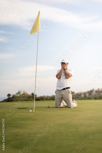Angry golfer lamenting for missing his shot on the green a few inches from the hole.