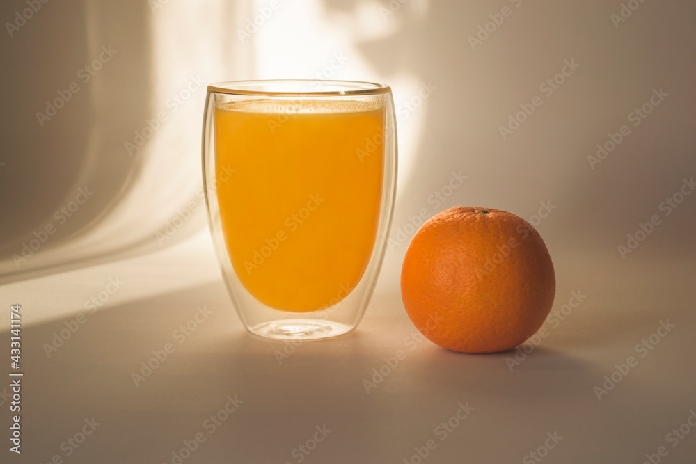 Glass of orange juice and orange on a light background in the shade Glass of orange juice and orange on a light background in the shade