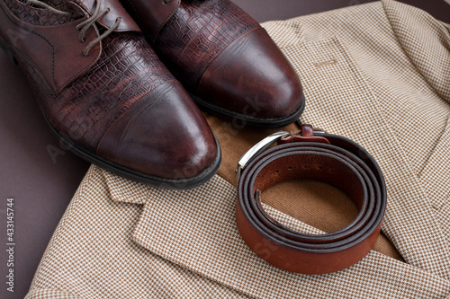 Flat lay of men dark brown derby shoes combined with light beige blazer and brown sweater and belt.
