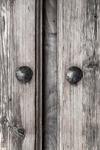 Black and white antique wooden door with nails and knots. Rustic and retro old door full of knots and scratches. Vintage wood texture surface, wood vein. Pareidolia, faces in wood grain.