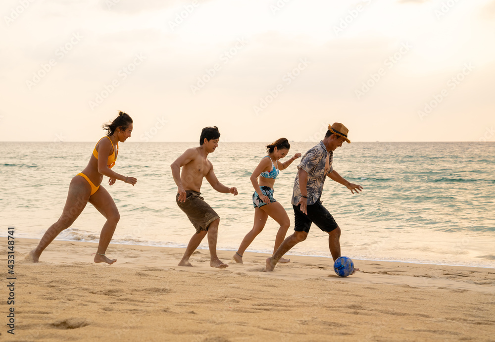 Group of Happy Asian man and woman friends playing beach soccer together on tropical beach in sunny day. Male and female friendship enjoy and having fun outdoor lifestyle activity on summer vacation