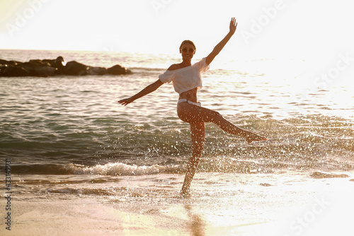 Fototapeta Naklejka Na Ścianę i Meble -  Beautiful caucasian woman playing in the water on the sandy beach at sunset sea shore.